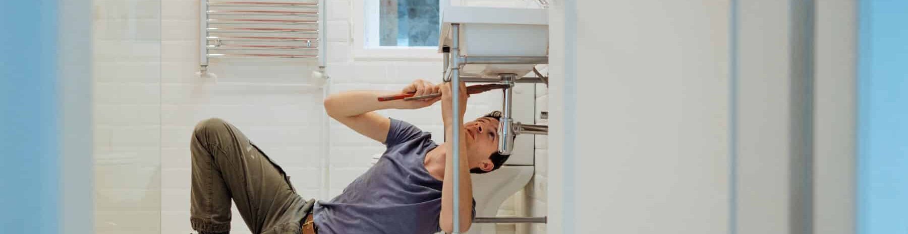 plumber using a pipe wrench to tighten a pipe under a sink