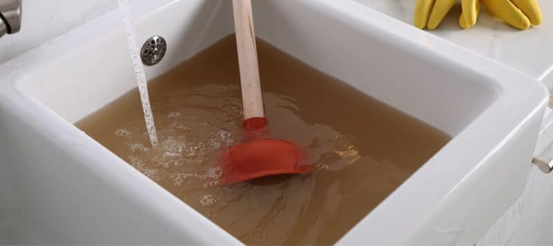 a wooden rubber plunger sitting in a clogged sink full of reddish brown water